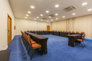 Un salón de conferencias con una larga mesa y sillas, alfombra azul y paredes blancas.