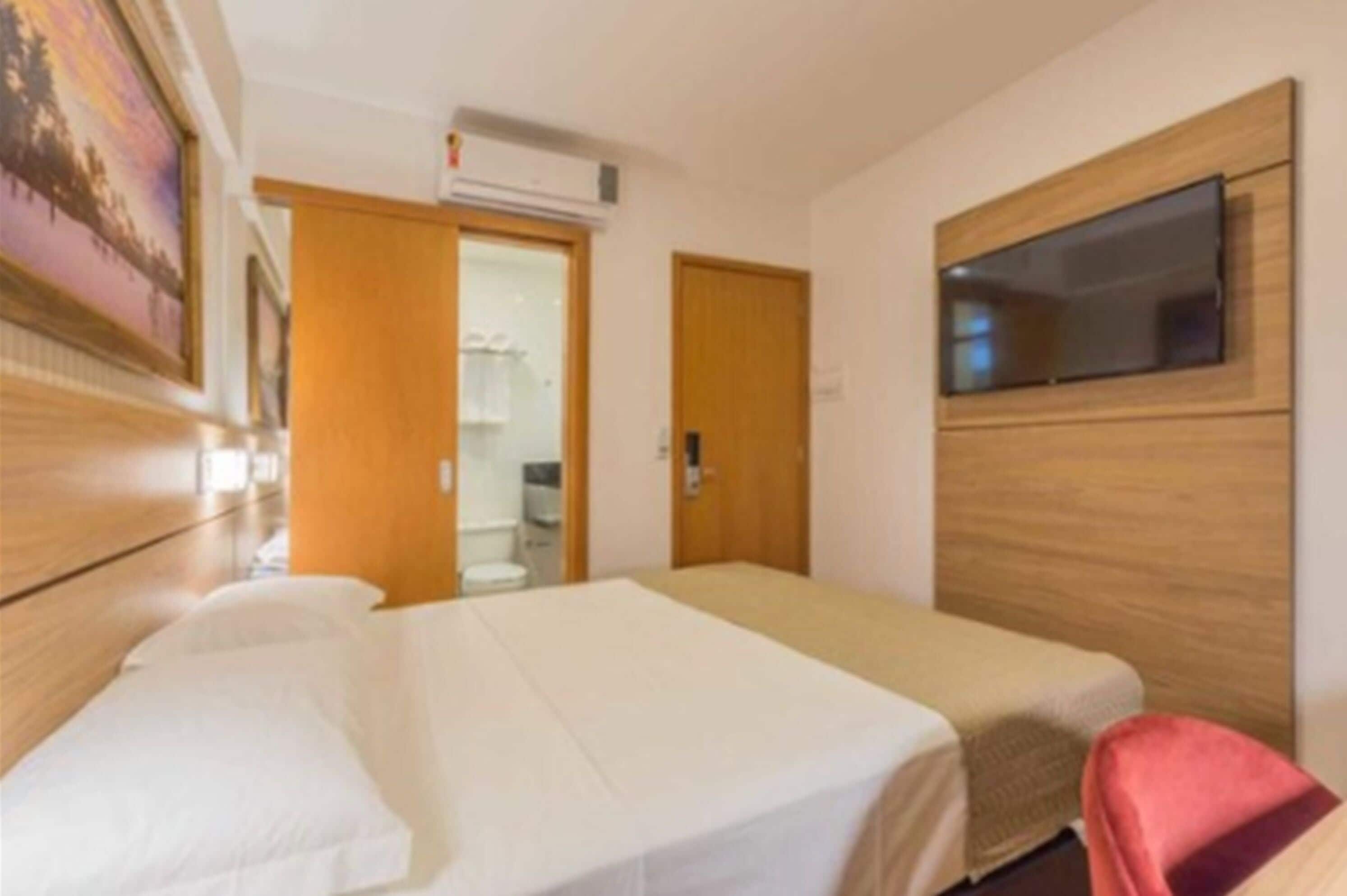 A hotel room with two single beds, a TV mounted on the wall, and a bathroom visible through an open door.