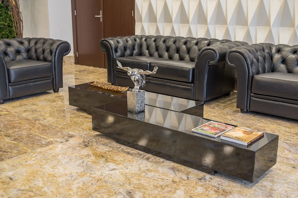 A modern lobby with a black leather sofa set, a glass coffee table with a metallic sculpture, and a marble floor. - Bristol Guararapes Hotel (Fortaleza)