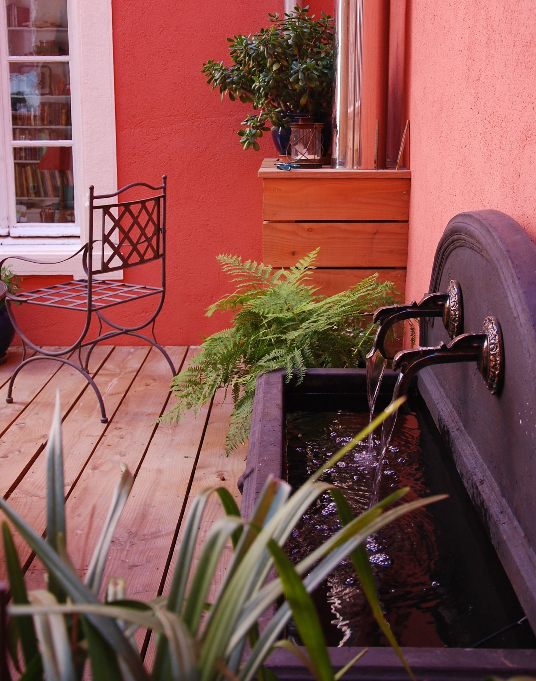 A wooden deck with a metal chair, a potted plant, and a water feature.