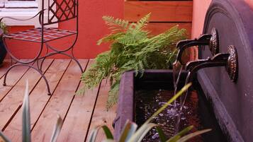 A wooden deck with a metal chair, a potted plant, and a water feature.