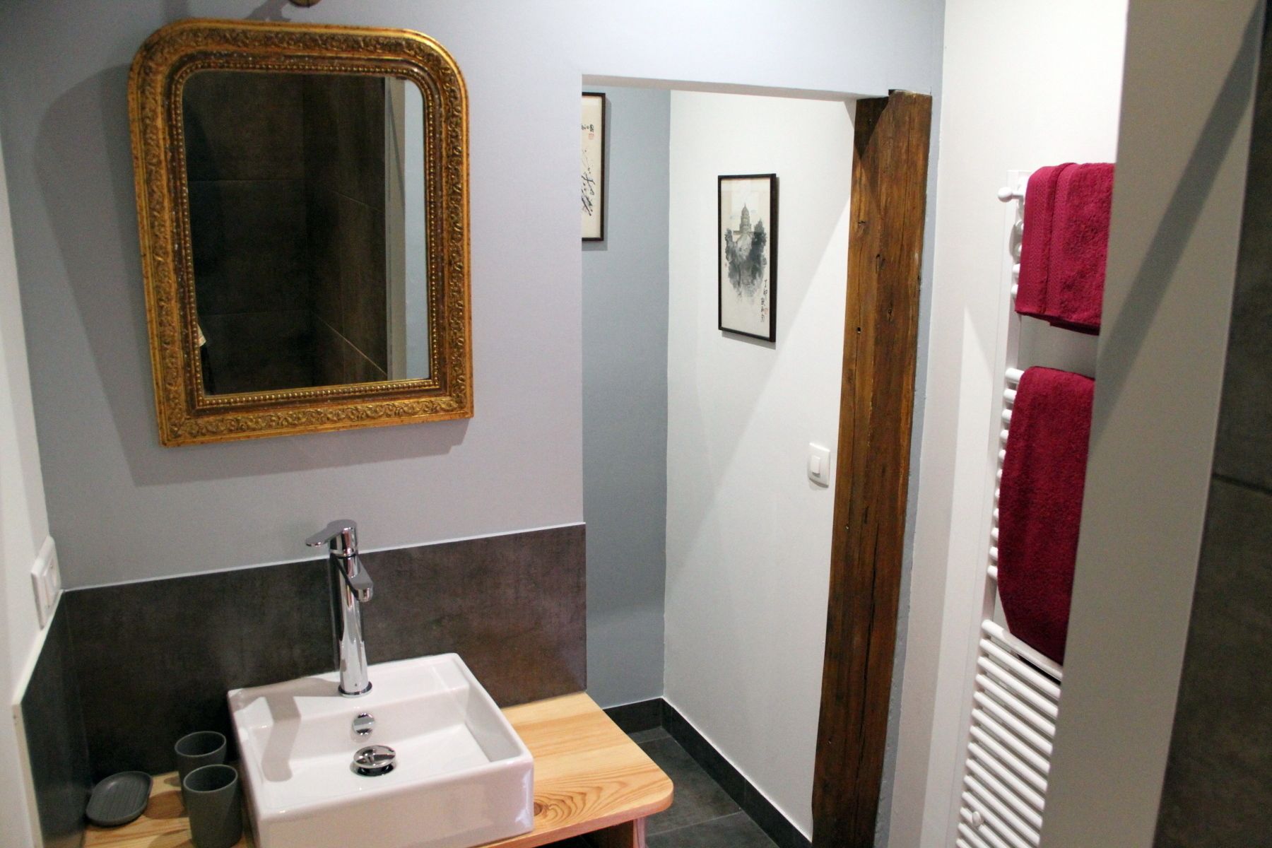 A bathroom with a white sink, a gold-framed mirror, and a wooden bench.