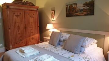 Un dormitorio con cama, almohadas, una mesita de noche, una lámpara, un armario de madera y un cuadro en la pared.