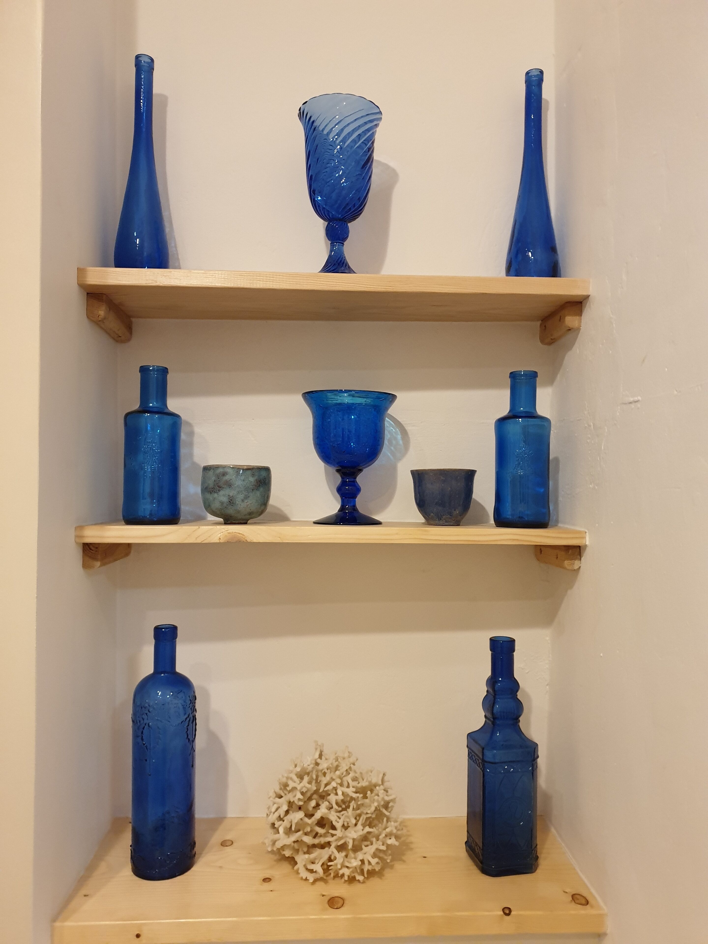 Blauwe glazen in een vitrine op houten planken, voor een effen muur.