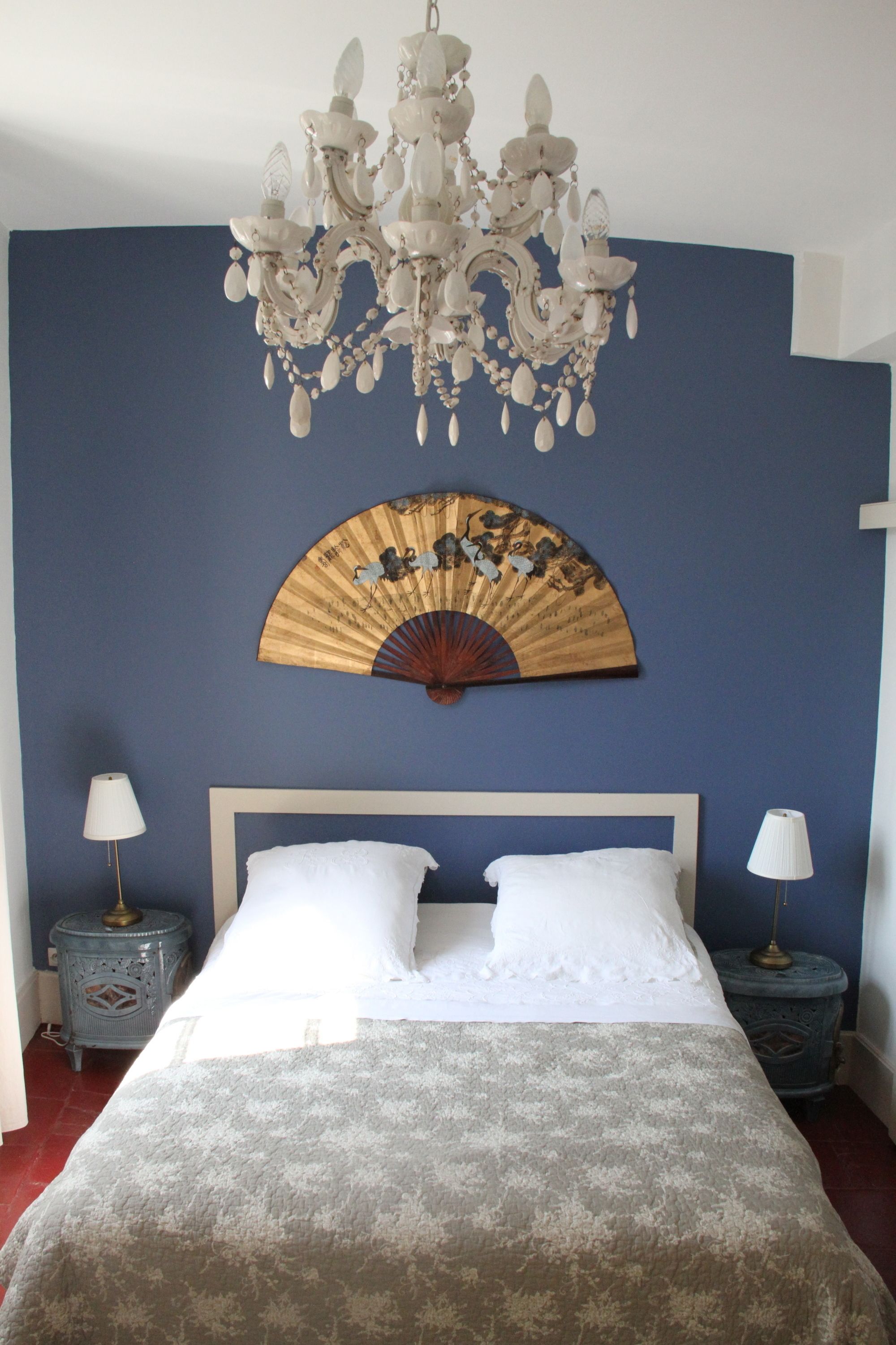 Een slaapkamer met een bed, twee nachtkastjes, een kroonluchter en een ventilator.