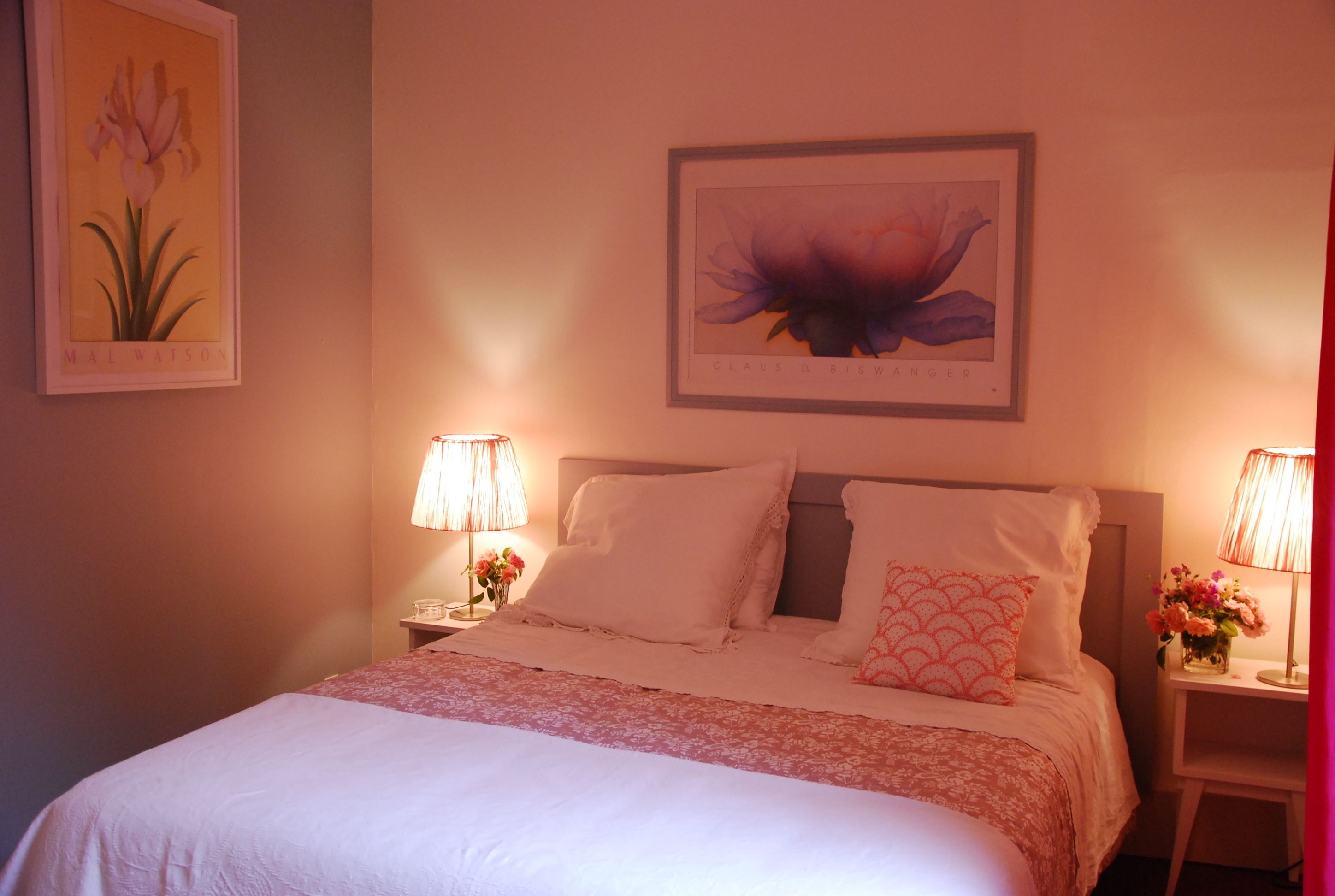 A neatly made bed with white linens and a pink floral bedspread, flanked by two bedside tables with lamps and floral arrangements.
