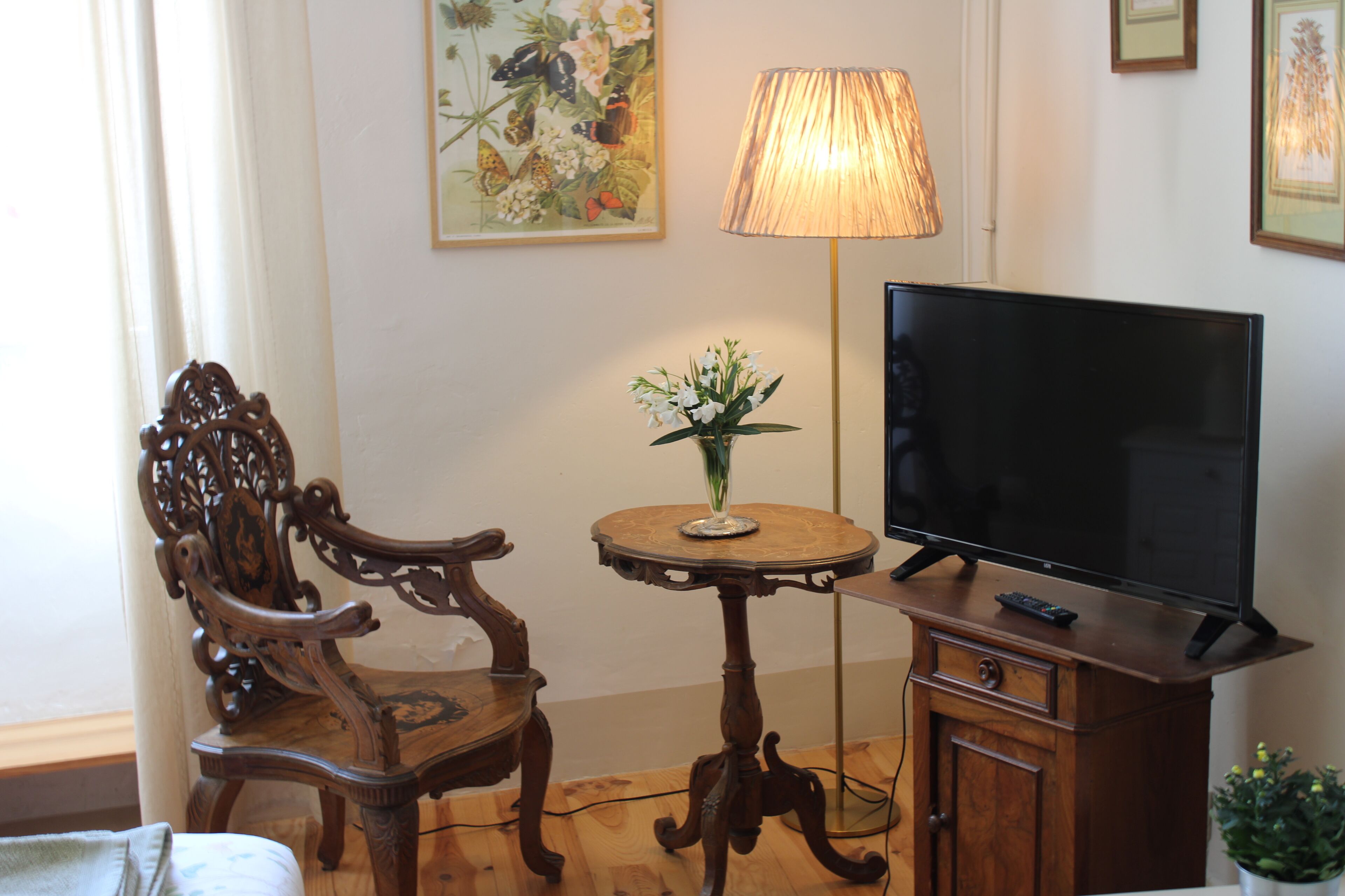A room with a wooden chair, a small table with a lamp, and a television on a wooden cabinet.