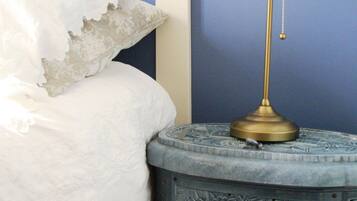 A bed with a white comforter and a decorative pillow, a brass table lamp on a blue side table with intricate carvings, and a blue wall in the background.