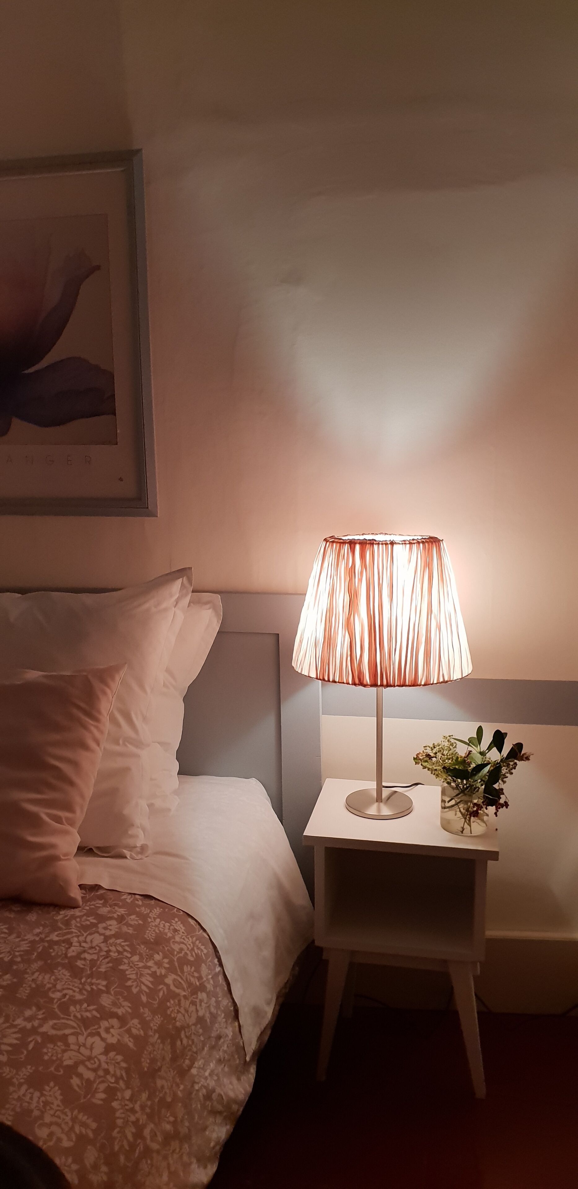 A bedroom with a bed, a bedside table with a lamp, and a framed picture on the wall.