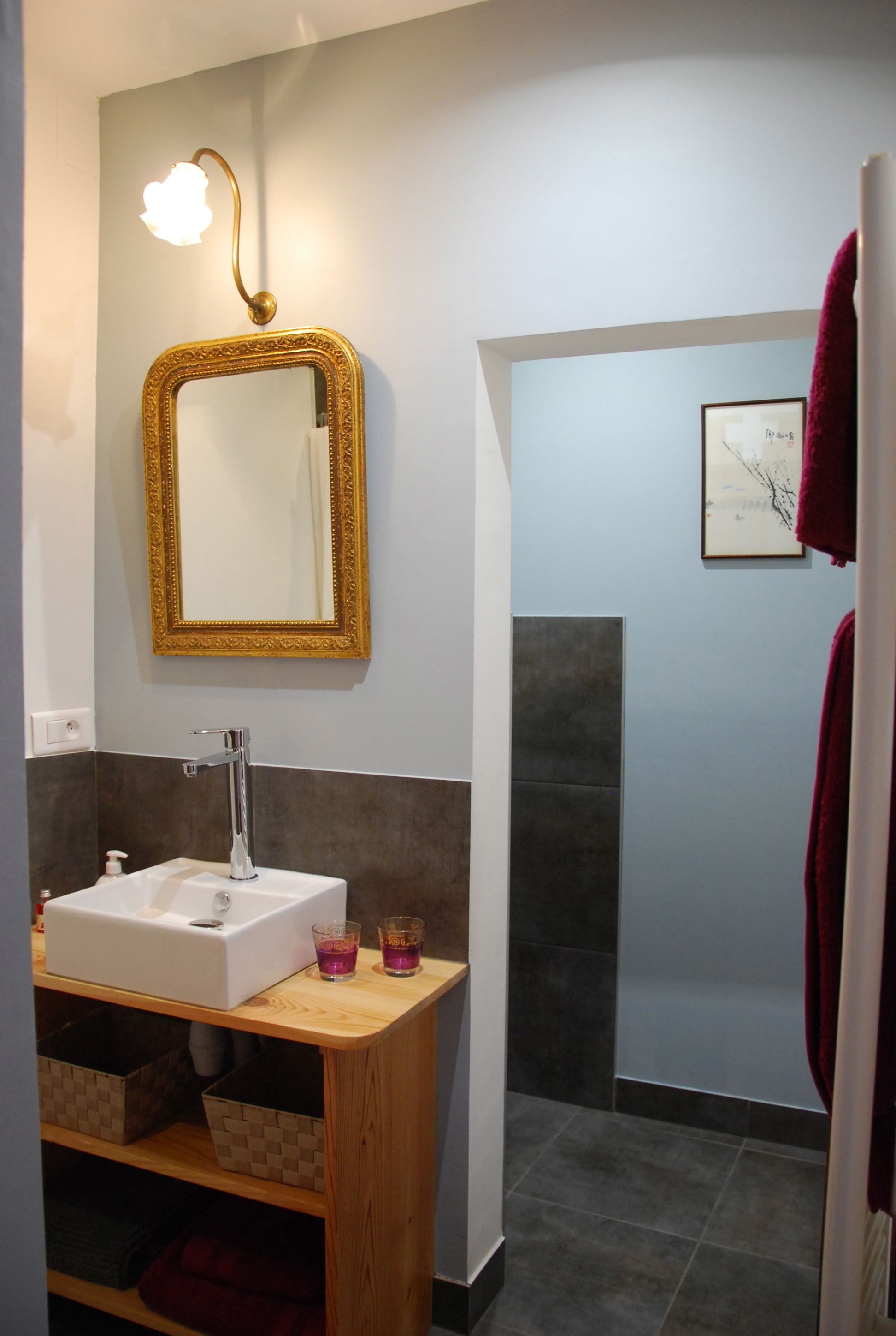 A bathroom with a white sink, a gold-framed mirror, a light fixture, and a framed picture on the wall.