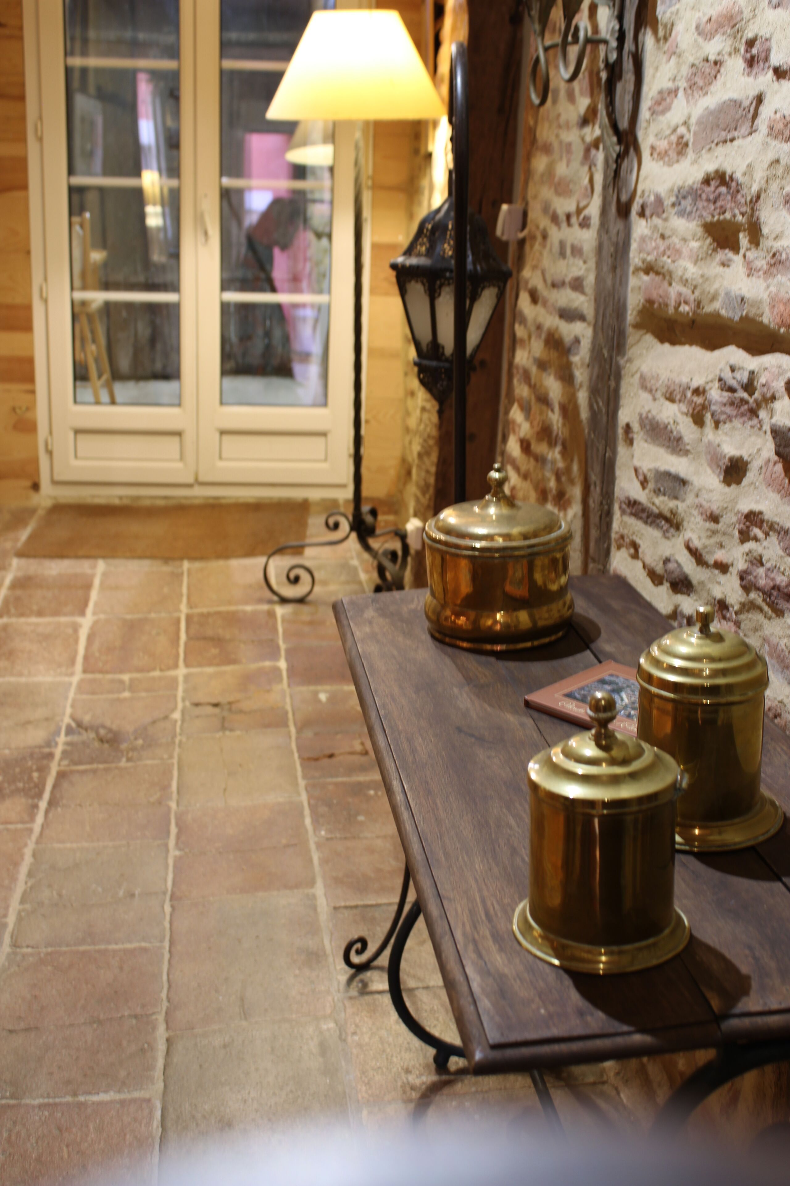 A wooden table with metal candle holders and a lamp, set against a brick wall with a door in the background.