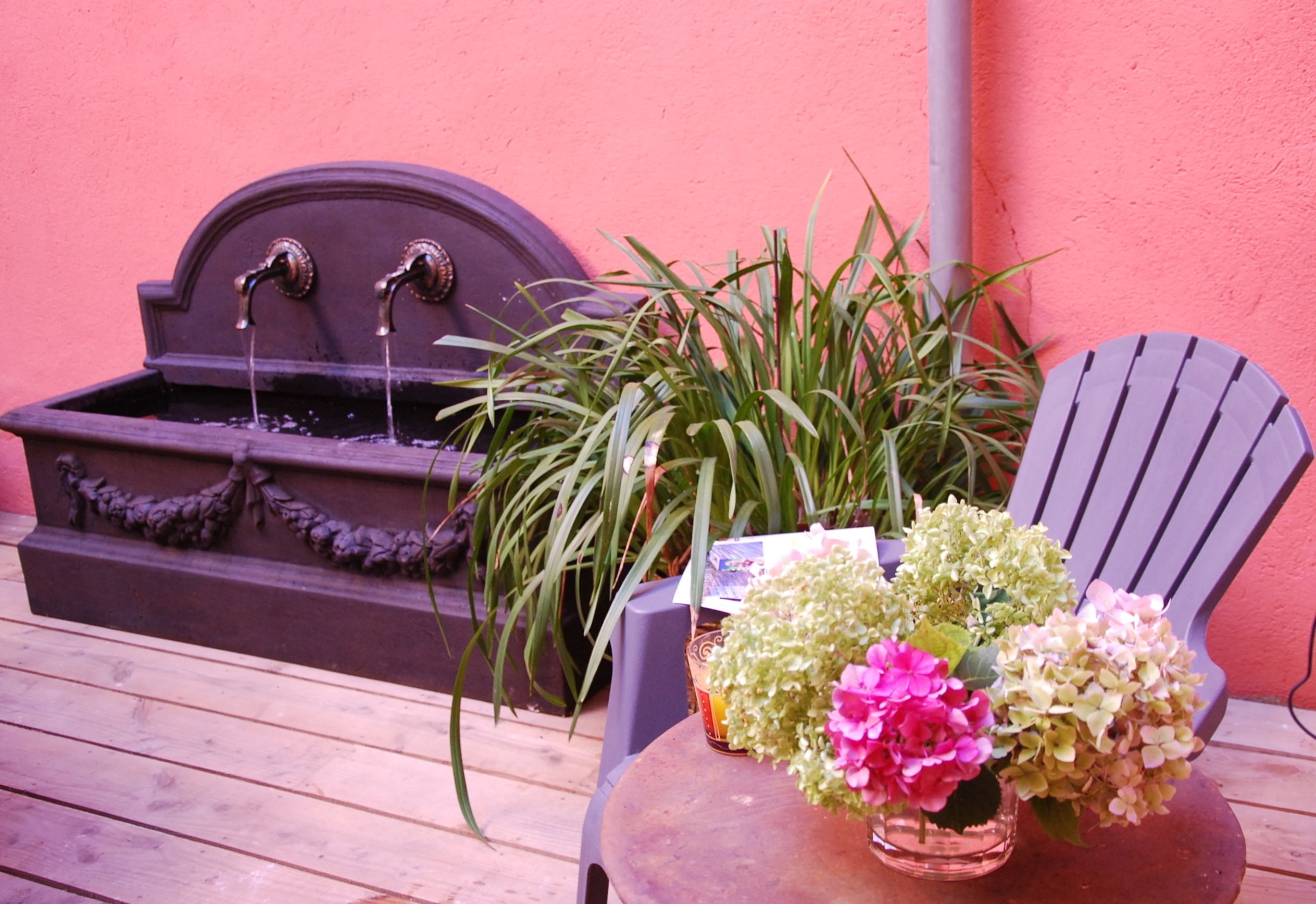 Un patio in legno con una piccola fontana, una sedia e un tavolo con un vaso di fiori.