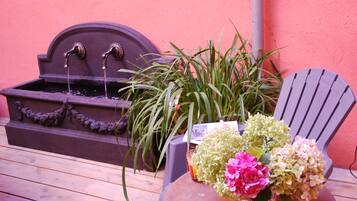 Un patio in legno con una piccola fontana, una sedia e un tavolo con un vaso di fiori.