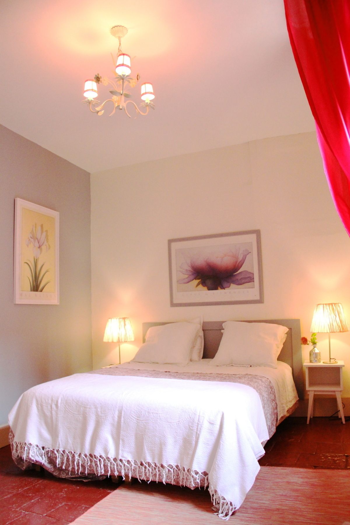 Un lit bien fait, avec du linge de lit blanc, une décoration murale à motifs floraux et un lustre.