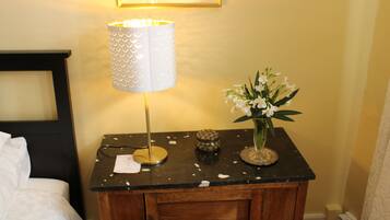 A wooden bedside table with a lamp, a vase with flowers, and a small decorative item.