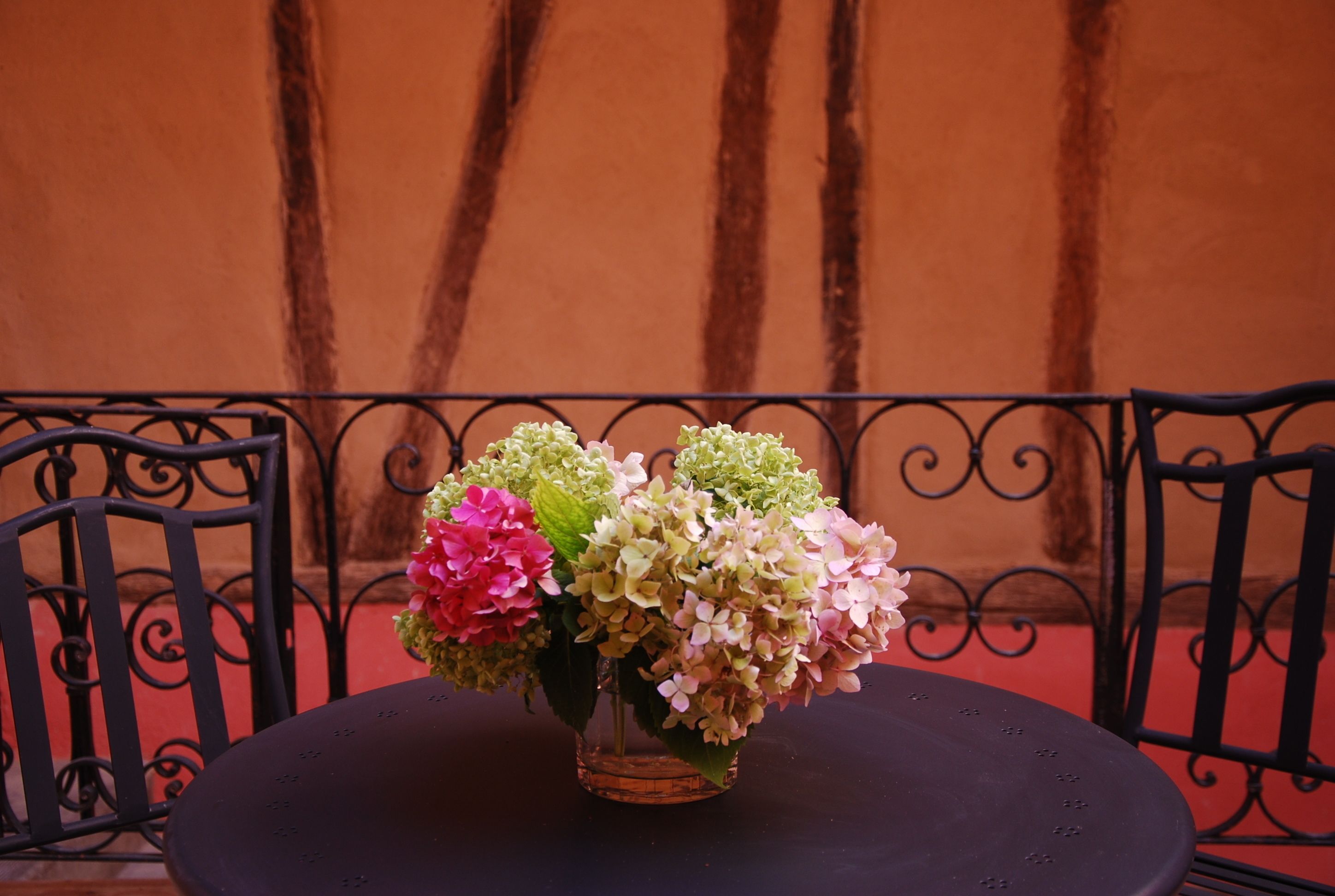 A round table with a vase of flowers in the center, surrounded by black metal chairs.