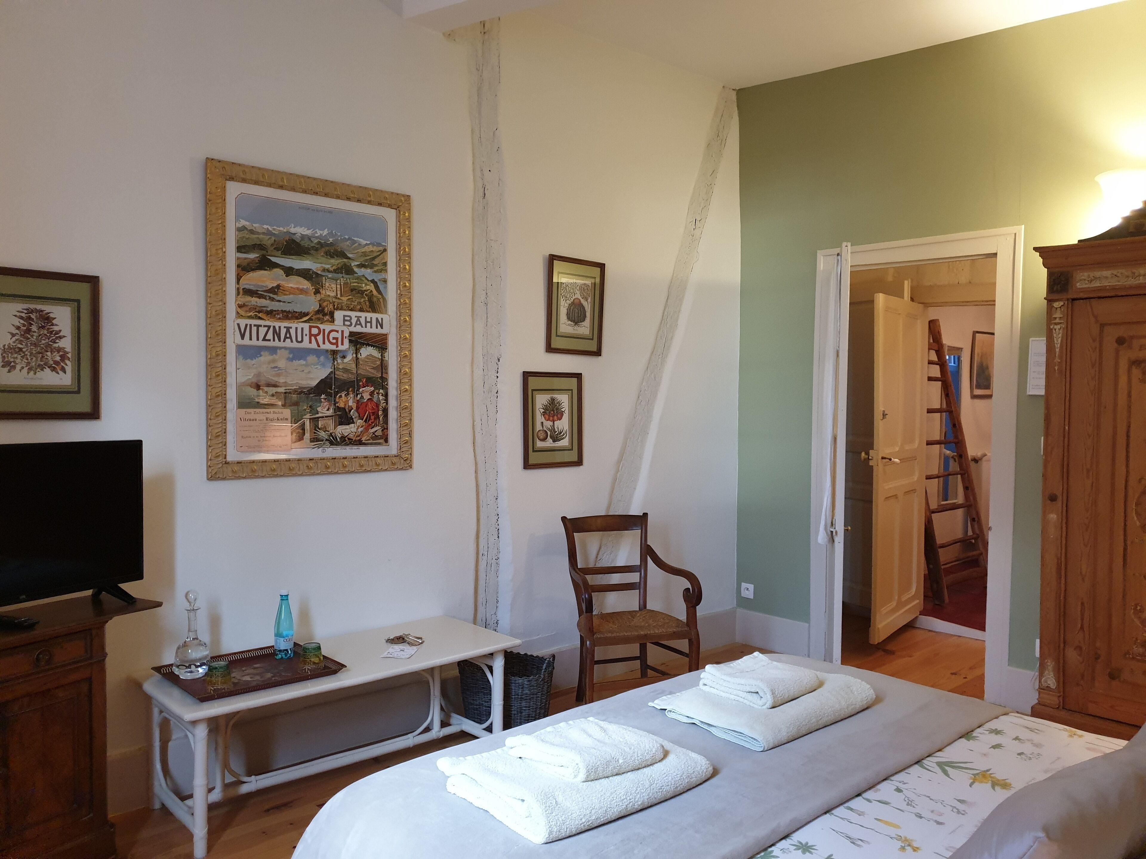 Een slaapkamer met een bed, een bureau, een stoel, een televisie en een deur die naar een andere kamer leidt.