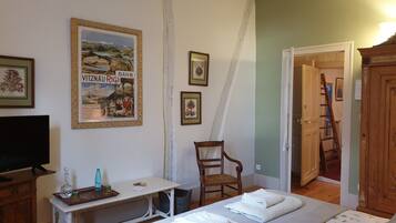 Een slaapkamer met een bed, een bureau, een stoel, een televisie en een deur die naar een andere kamer leidt.