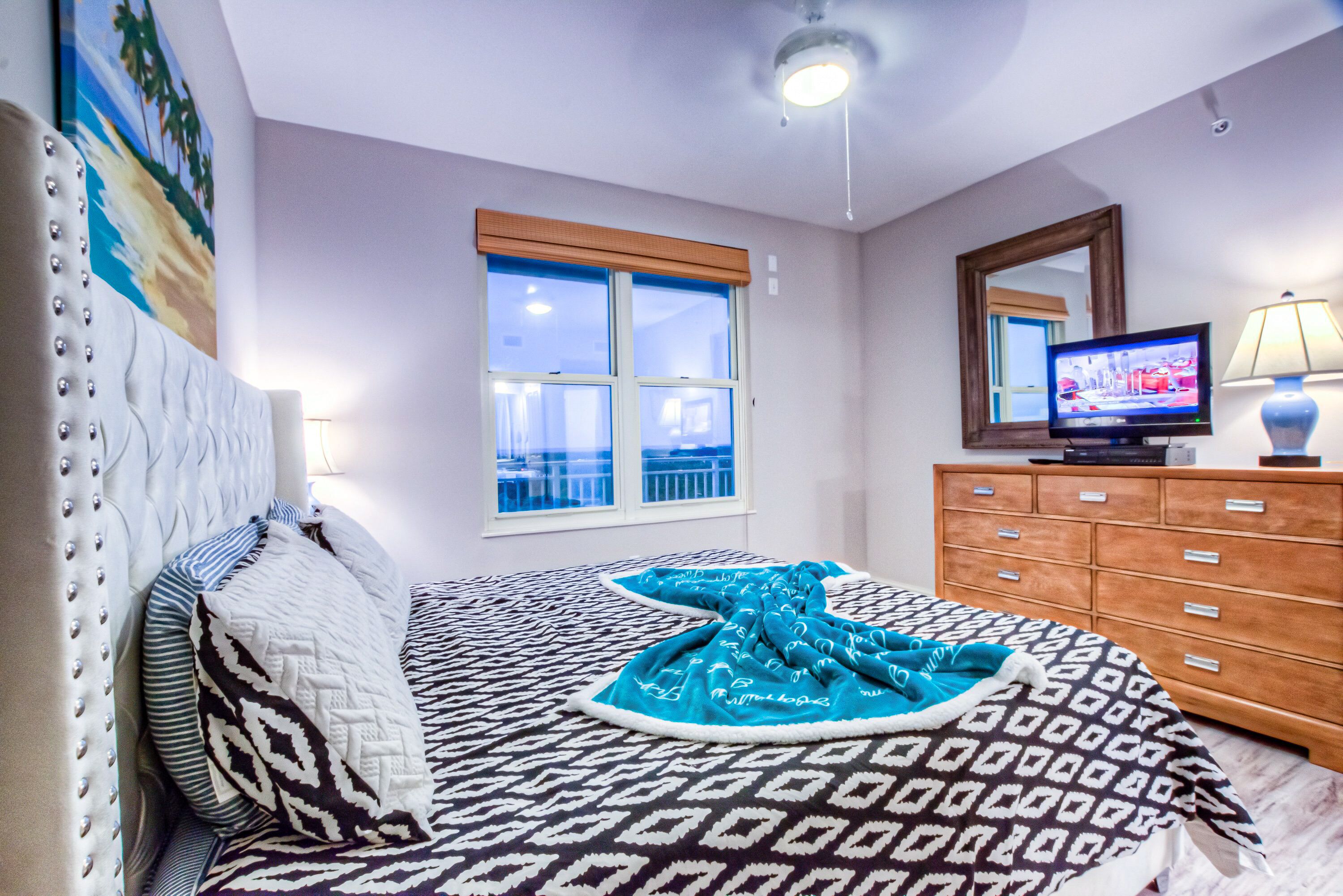 A bedroom with a bed, a television, a dresser, and a window with a view.