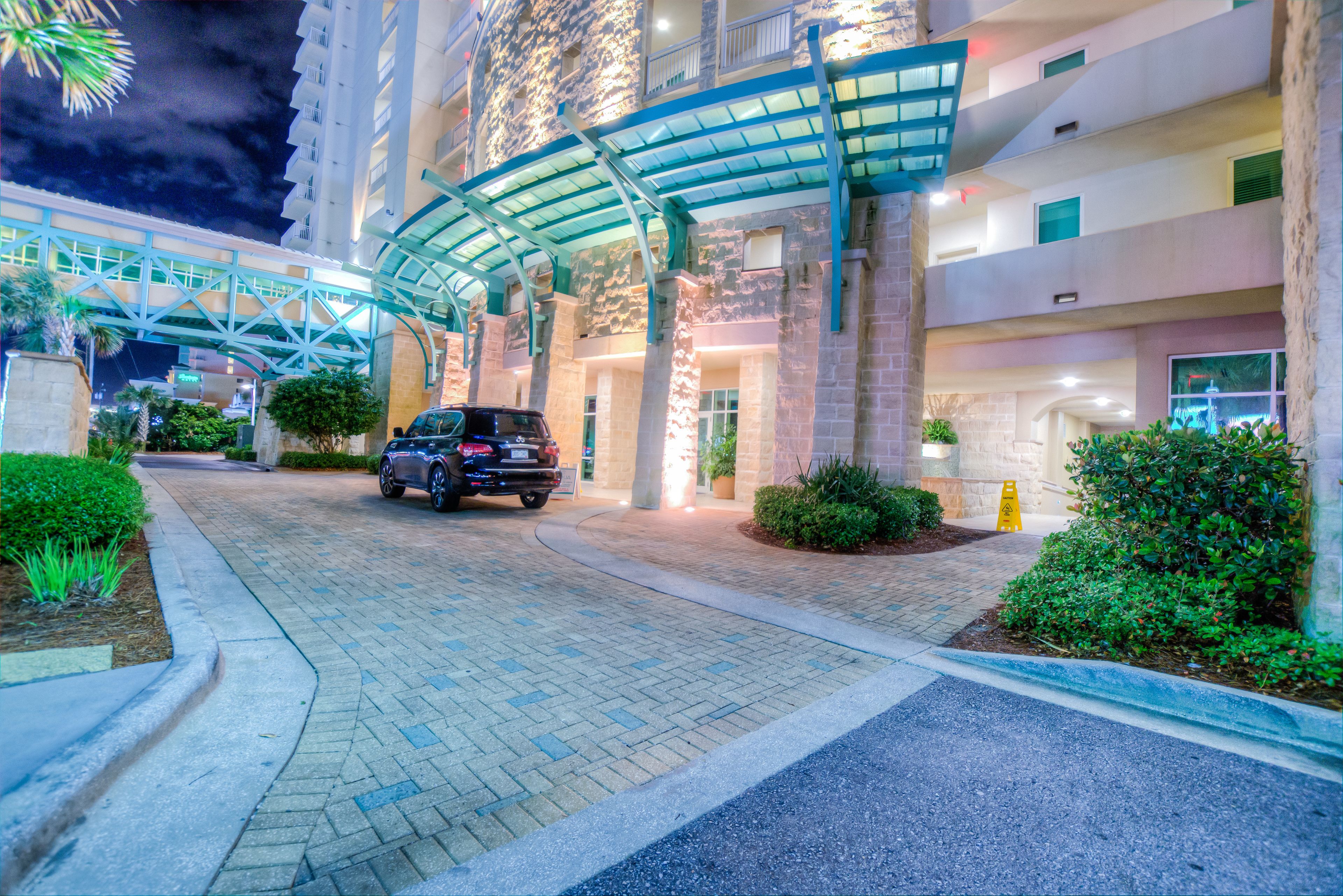 A hotel entrance with a covered walkway, paved driveway, and greenery.