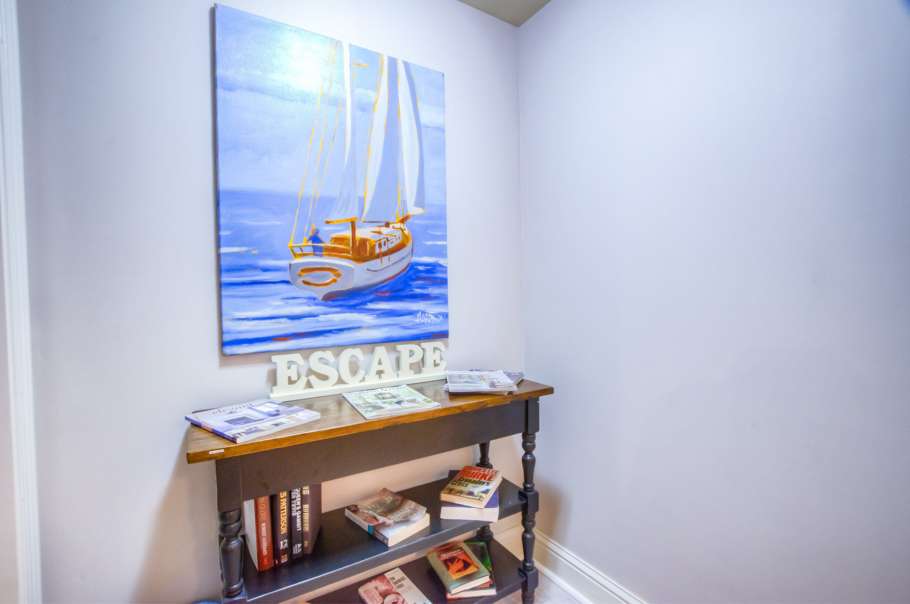 Een kamer met een boekenkast, een schilderij van een zeilboot en een bord waarop 'ESCAPE' staat.