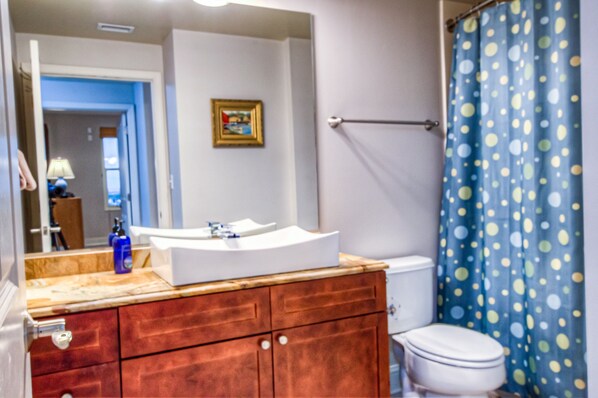 A bathroom with a wooden vanity, a white sink, a toilet, and a shower curtain with polka dots.