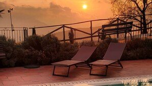 Vista al atardecer con piscina, sillones de descanso y un banco de madera.