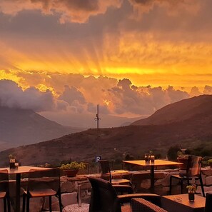 An outdoor seating area with tables and chairs, a parking sign, and a mountainous backdrop during sunset.