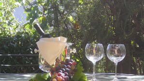 A table with a glass container, two wine glasses, and a bunch of grapes.