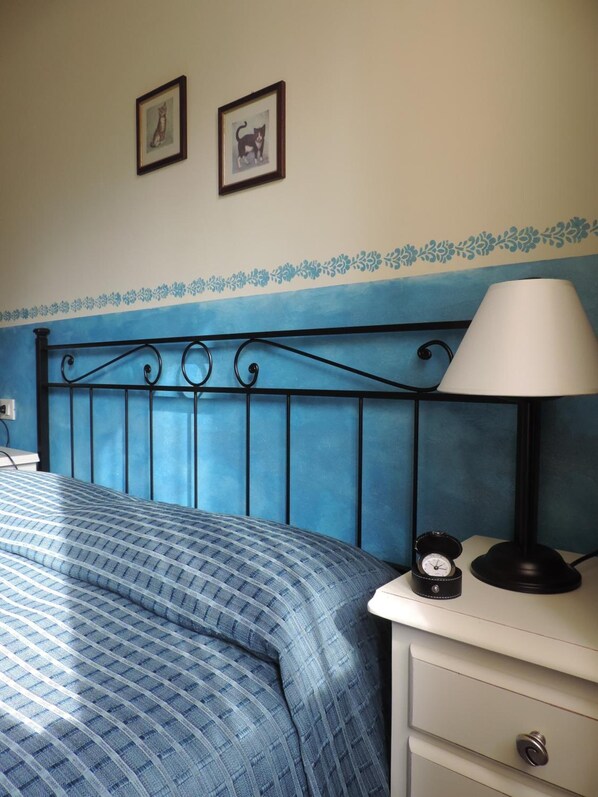 Un dormitorio con cama, mesita de noche, lámpara y dos cuadros en la pared.