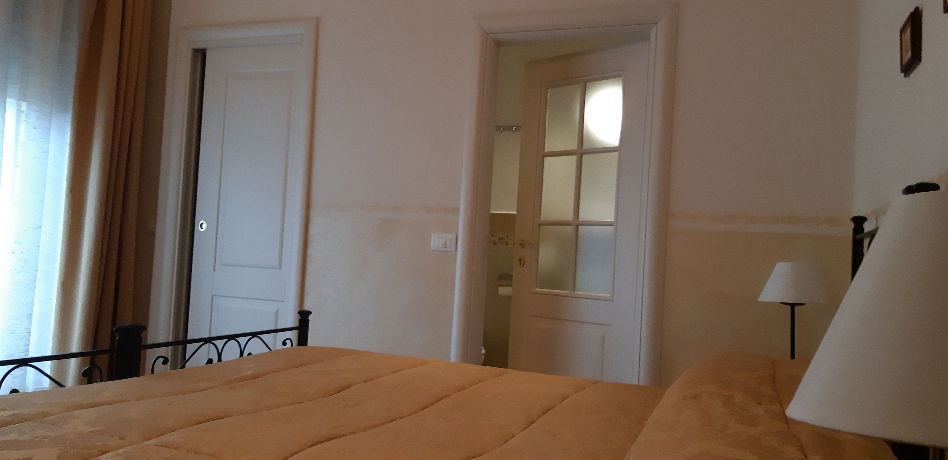 A bedroom with a bed, a lamp, and a door leading to another room.