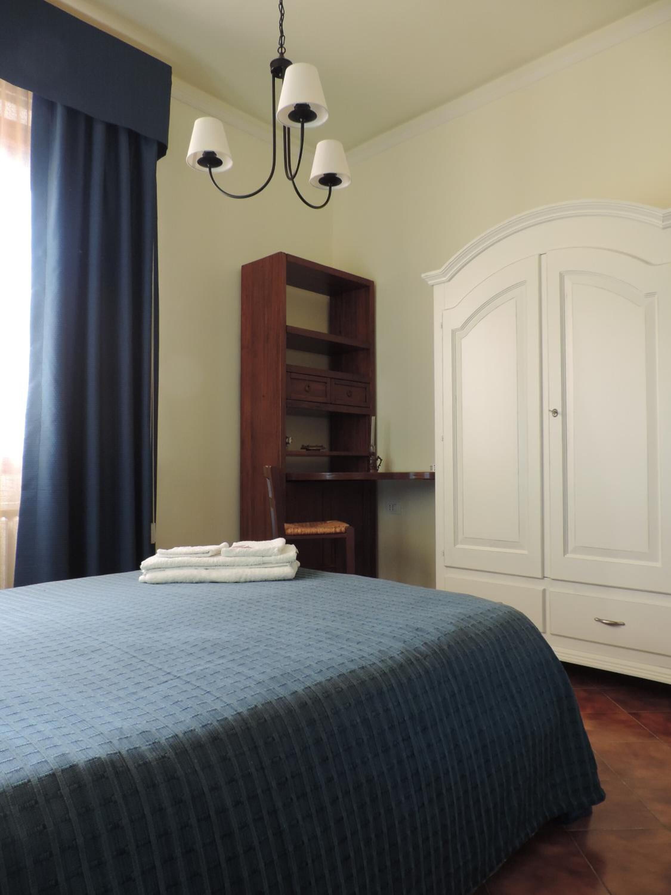 A bedroom with a bed, a wardrobe, a shelf unit, and a chandelier.
