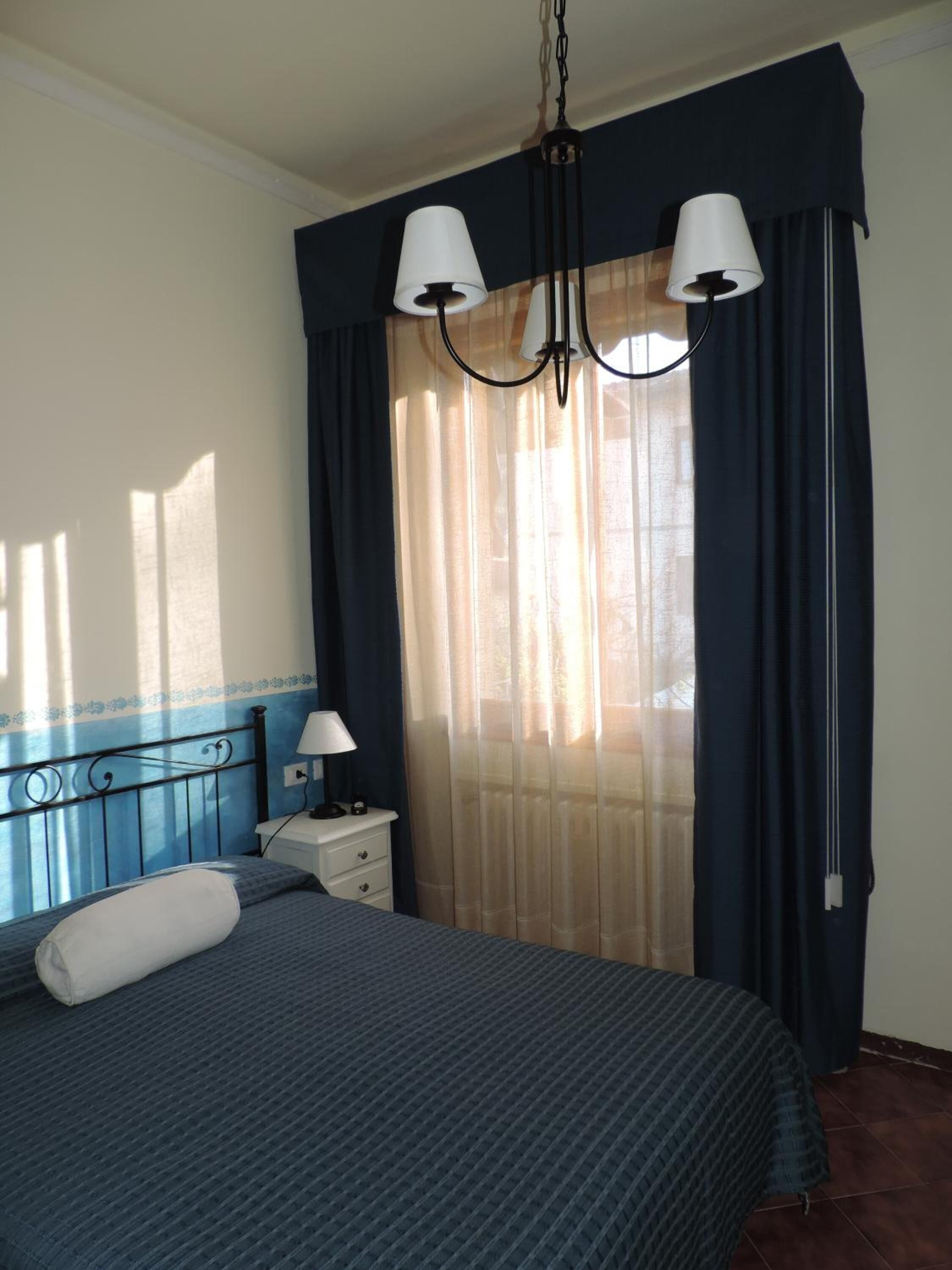 A bedroom with a bed, two bedside lamps, a nightstand, and a window with curtains.