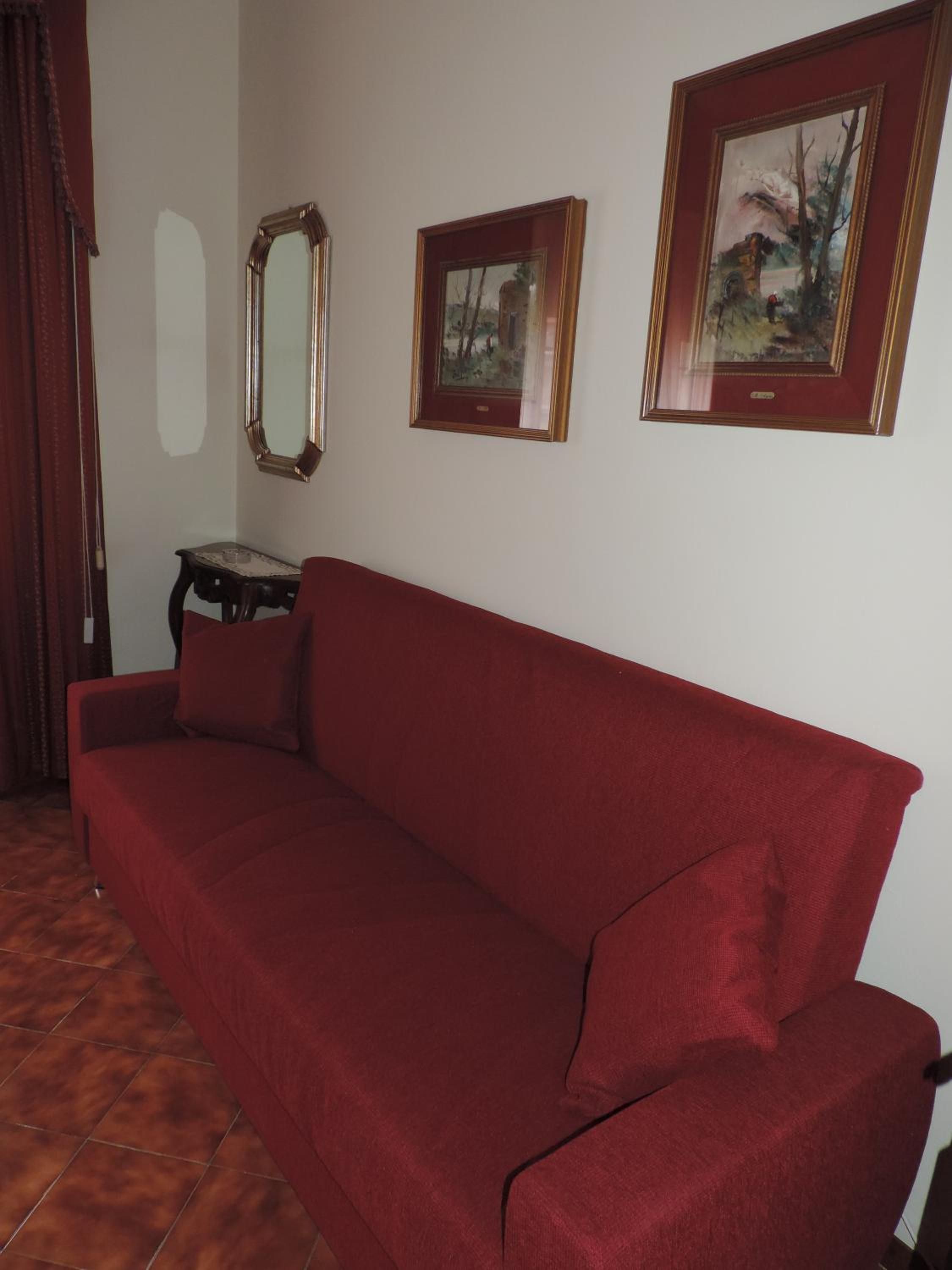 A red sofa in a room with a tiled floor, a small table, and three framed pictures on the wall.