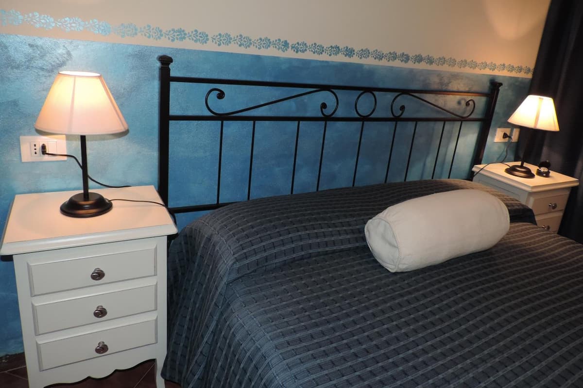 A bedroom with a bed, two bedside tables with lamps, a dresser with drawers, and a decorative wall border.