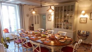 A dining room with a round table set for a meal, surrounded by white chairs with red cushions. - Les Chaufourniers (Crouay)
