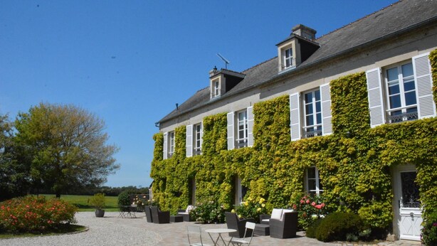 A two-story building with a garden patio area featuring outdoor seating. - Les Chaufourniers (Crouay)