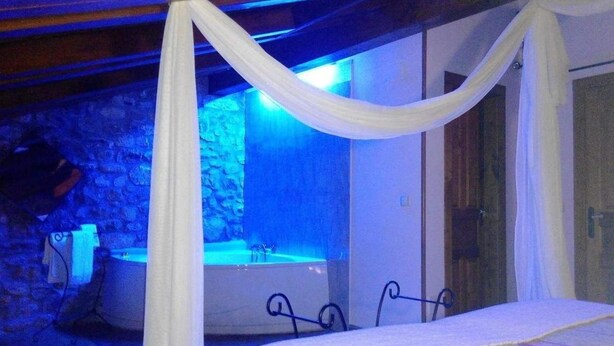 A bedroom with a bed, a bathtub, and a stone wall. - Posada Solar Montero de la Concha (Santa Maria de Cayon)
