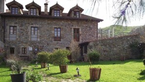 A stone building with multiple windows and a garden with potted plants and a stone pathway. - Posada Solar Montero de la Concha (Santa Maria de Cayon)