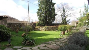 A stone pathway leading through a garden with a stone wall, potted plants, and a large tree. - Posada Solar Montero de la Concha (Santa Maria de Cayon)