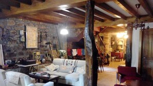 A cozy living room with a stone wall, a wooden ceiling, a white sofa, a red plaid chair, and a wooden pillar. - Posada Solar Montero de la Concha (Santa Maria de Cayon)