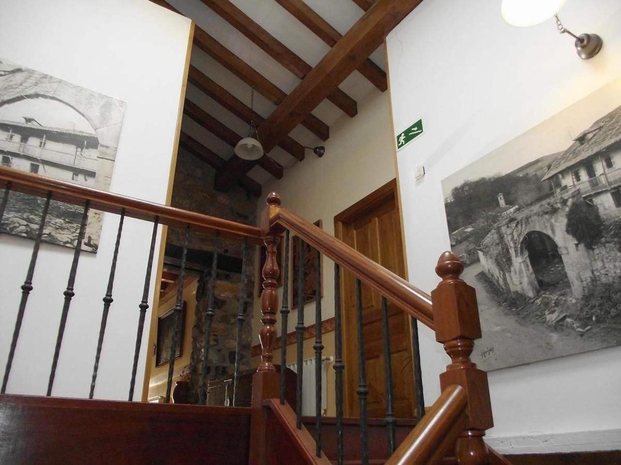 A wooden staircase with a metal railing, a stone wall, and a black and white photograph on the wall.