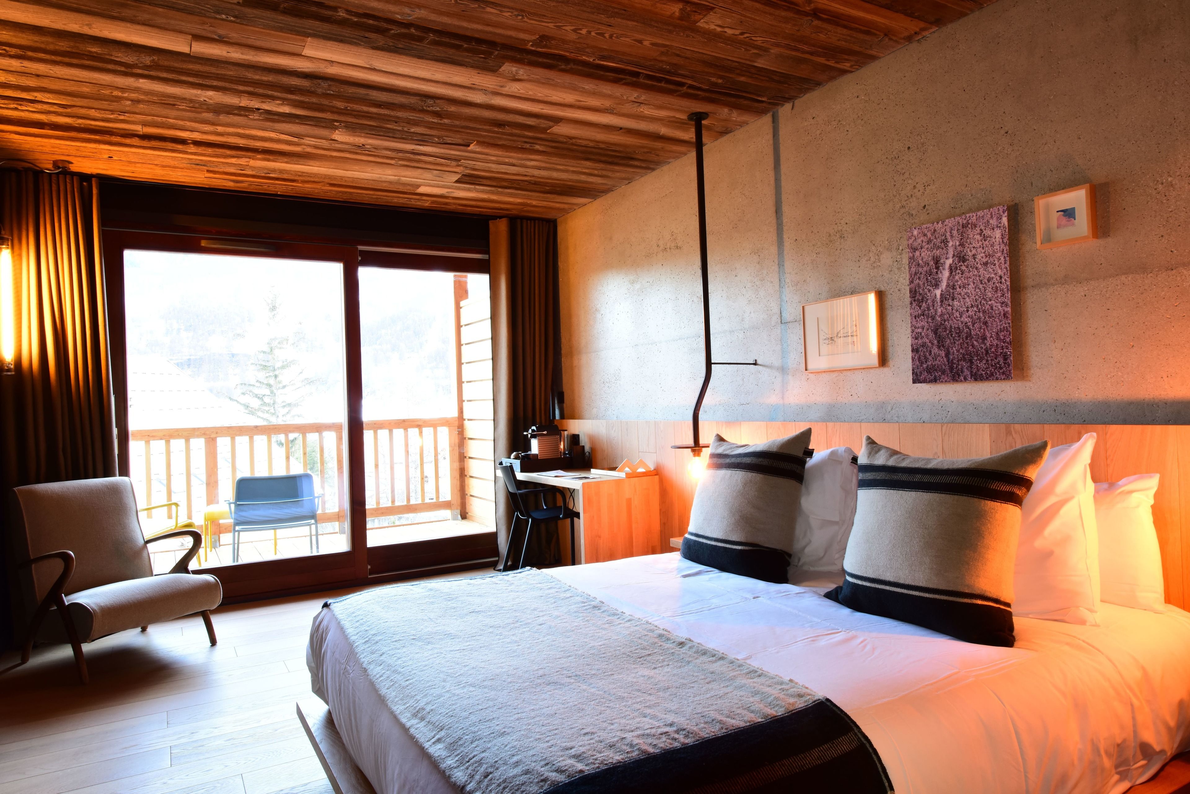 A hotel room with a large bed, a desk, a chair, and a view of a balcony.
