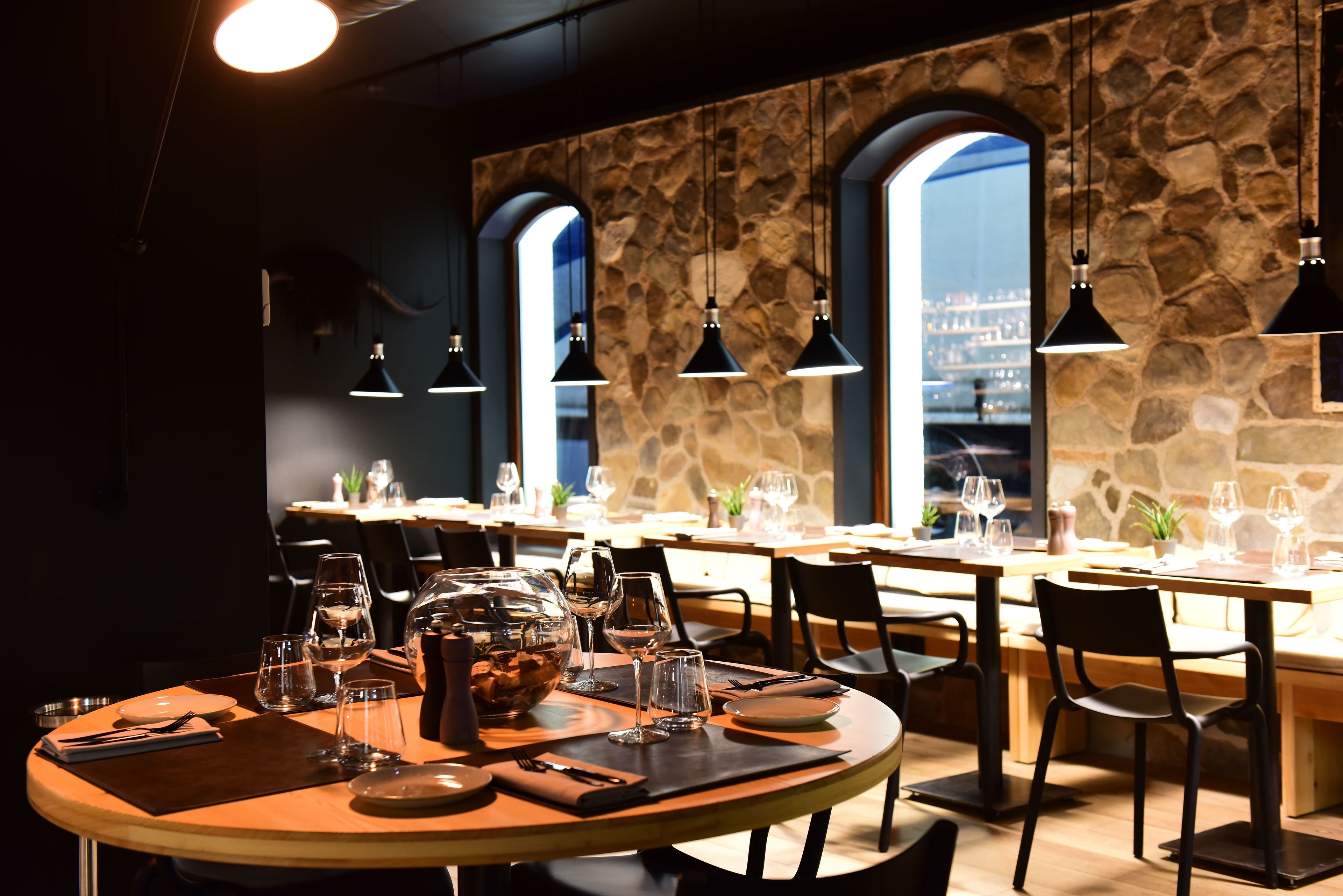 A restaurant with round tables, black chairs, and stone walls.