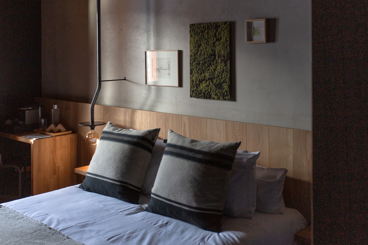 Cama bem arrumada com duas almofadas, cabeceira de madeira e uma obra de arte pendurada na parede.