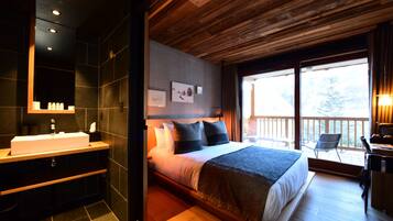 Une chambre moderne avec un grand lit, un plafond en bois, une salle de bain avec un lavabo et un balcon avec vue.