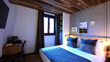 Una camera da letto con soffitto in legno, un letto con coperta blu, un comodino con una lampada e una finestra con tende.