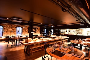 Un restaurant doté de nombreuses tables et chaises, de murs en pierre et de grandes fenêtres.