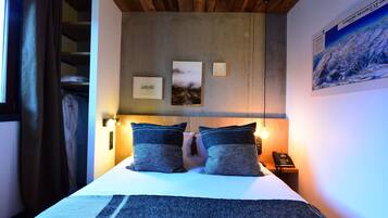 A bedroom with a bed, two pillows, a nightstand with a phone, and a painting on the wall.
