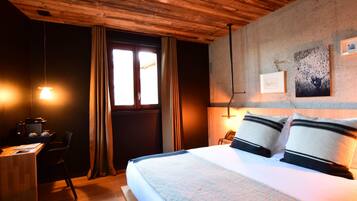 Habitación de hotel con techo de madera, cama con almohadas, escritorio con silla y ventana con cortinas.